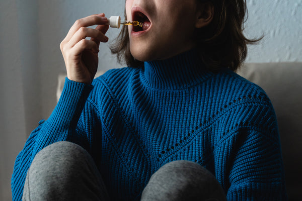 Woman in a blue sweater dropping CBD tincture in her mouth