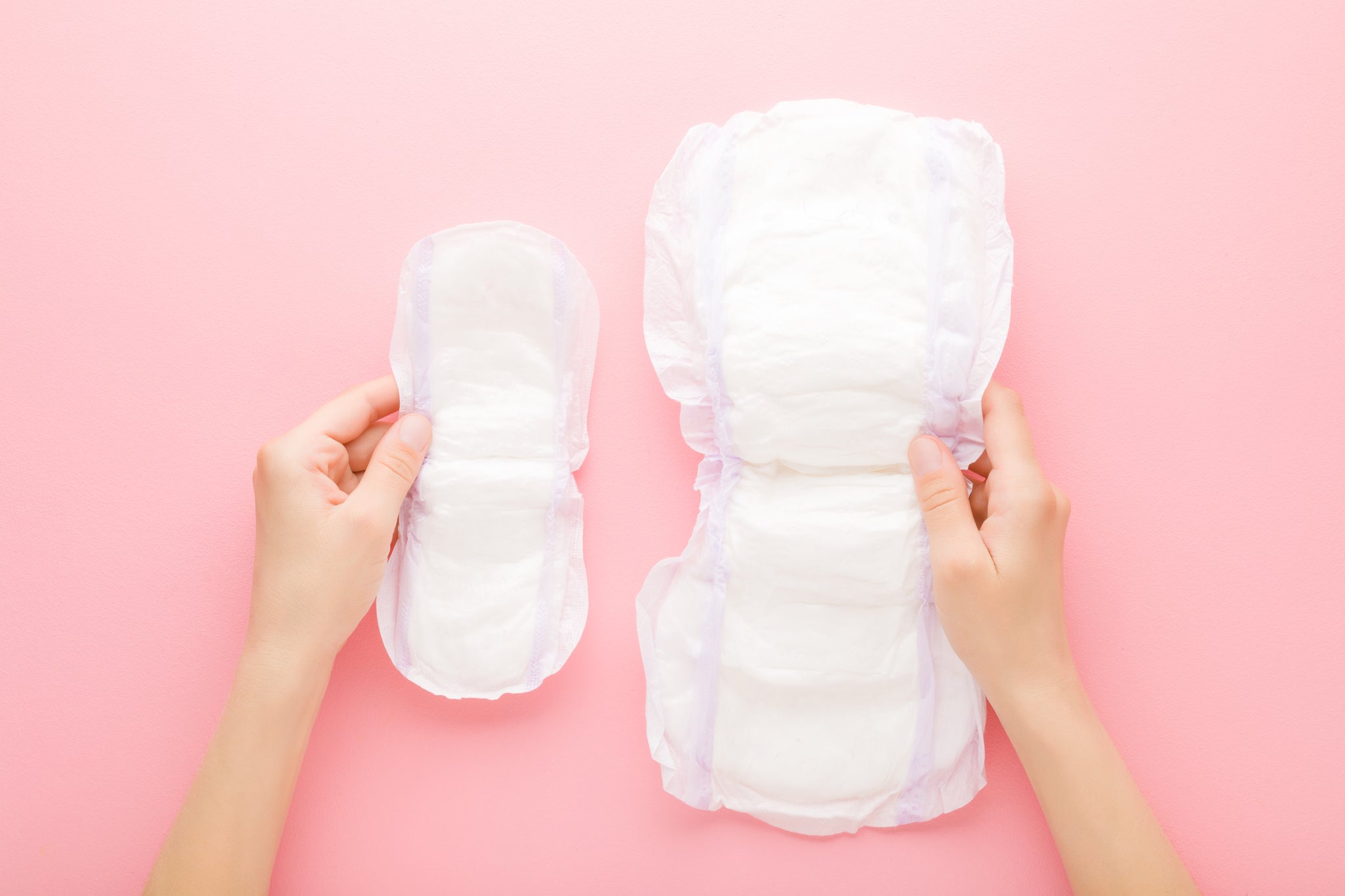 woman hands holding opened white sanitary towels on pink table background. Big and small size. Pastel color. Hygiene product for urinary incontinence or after childbirth. Top down view.