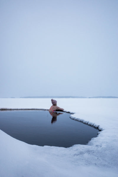 Frau mit heller Mütze in einem gefrorenen See schwimmend 