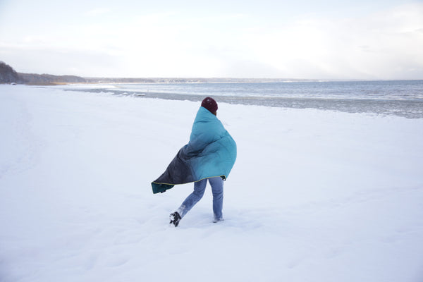 Frau mit roter Mütze läuft in eine Decke gewickelt durch den Schnee