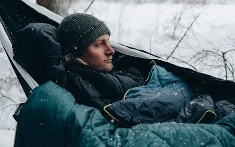 Mann liegend in schwarzer HÄNG Hängematte mit blauer DÄCKE Campingdecke im Schnee