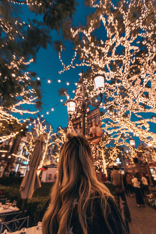 blonde Frau schaut auf Lichterketten im Baum auf einem Weihnachtsmarkt