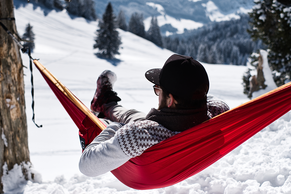 Mann in HÄNG Hängematte liegend im Winter mit Schnee im Hintergrund 
