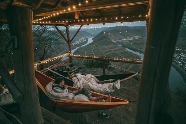 zwei Männer liegen in HÄNG Hängematten in einem beleuchteten Pavillon mit Ausblick auf eine Landschaft 