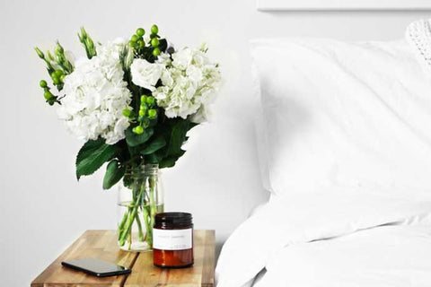 Flowers displayed on bedside cabinet next to bed with white sheets