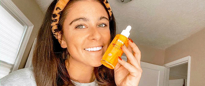 Woman holding face oil next to her skin