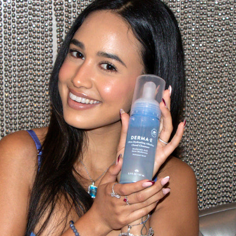 Influencer holding up a blue bottle of DERMA E hydrating cloud cleanser