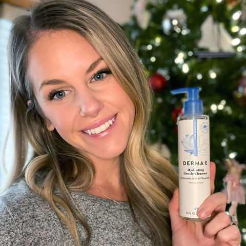 Influencer holding a bottle of DERMA E ultra hydrating cleanser in front of christmas tree