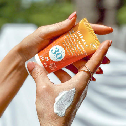 hands holding bottle of DERMA E spf 30 clear mineral zinc sunscreen