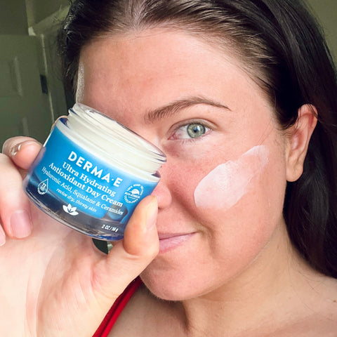 Woman with blue eyes holding blue glass jar of hydrating day cream derma e