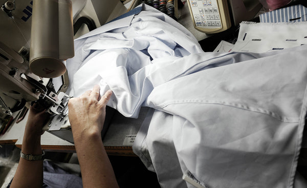 tailor in workshop stitching white custom men's dress shirt