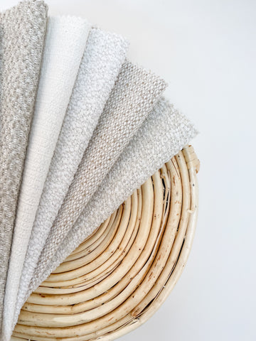 Beautifully displayed white upholstery fabrics fanned out on a circular bamboo-style basket bottom