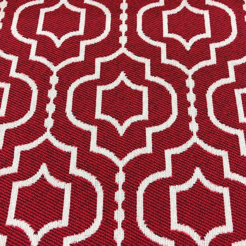 Close-up view of a geometric-patterned upholstery fabric with a bold red background and white interconnected diamond and quatrefoil shapes. The design has a raised texture, suggesting a jacquard weave, which adds dimension and a luxurious feel to the fabric.