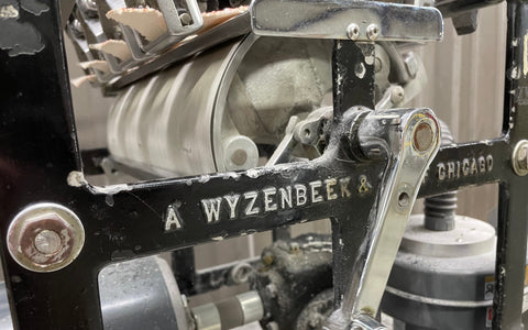 ALT Text: "A close-up image of a Wyzenbeek abrasion tester, with metal components labeled 'A WYZENBEEK & STAFF CHICAGO.' The machinery is partially in motion, illustrating the testing process for fabric durability.