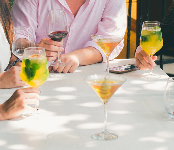 Mehrere Frauen sitzen an einem Tisch auf dem sieben Cocktail Gläser stehen.