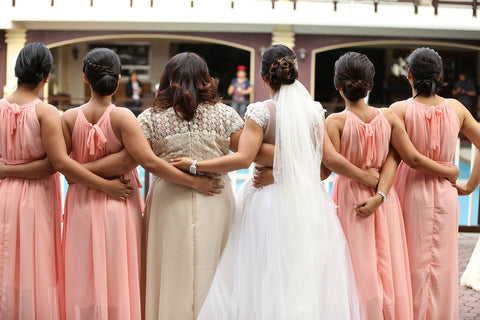 Eine Braut im weißen Brautkleid ist links und recht umgeben von ihren Brautjungfern in apricot-farbenen Kleidern und ihrer Mutter.