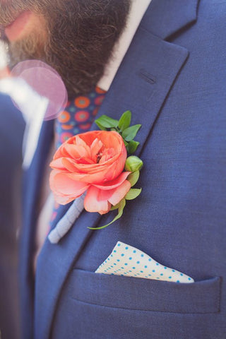 Eine Nahaufnahme eines blauen Anzugs mit einem Einstecktuch und einer Ansteckblume in der Pantonefarbe 2019 Living Coral.