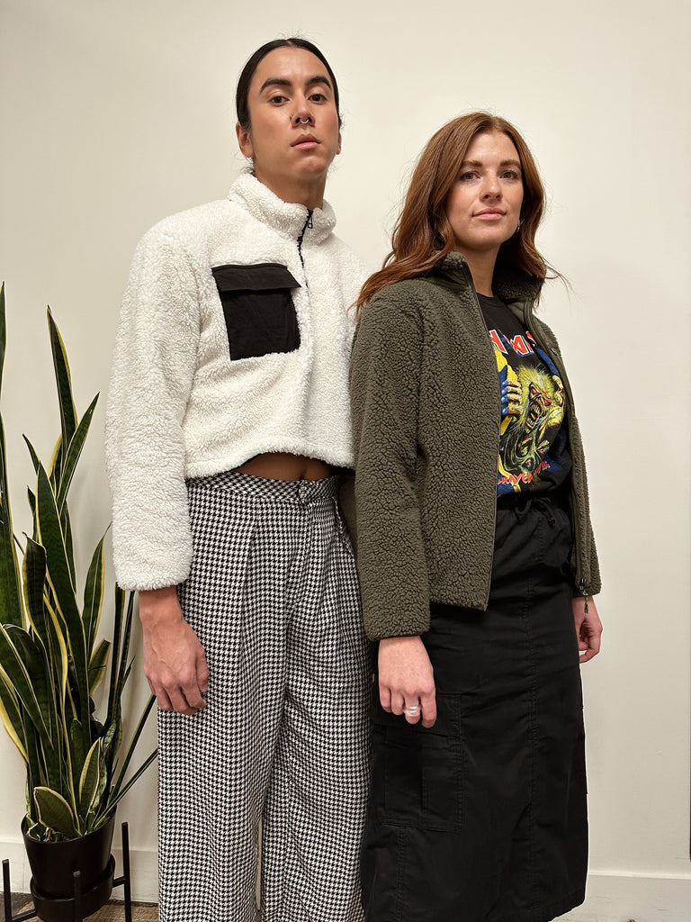 Two people stand wearing a white and a army green fleece sweater