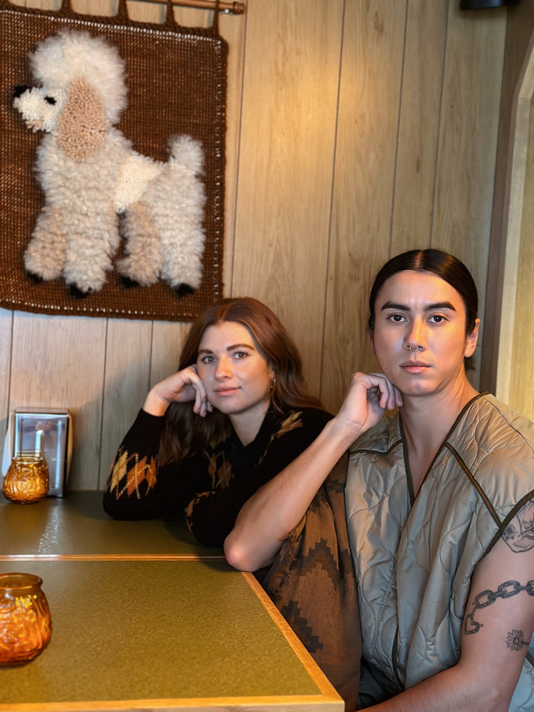 Two people sit in a booth at Class Clown restaurant in front of a poodle tufted piece of art