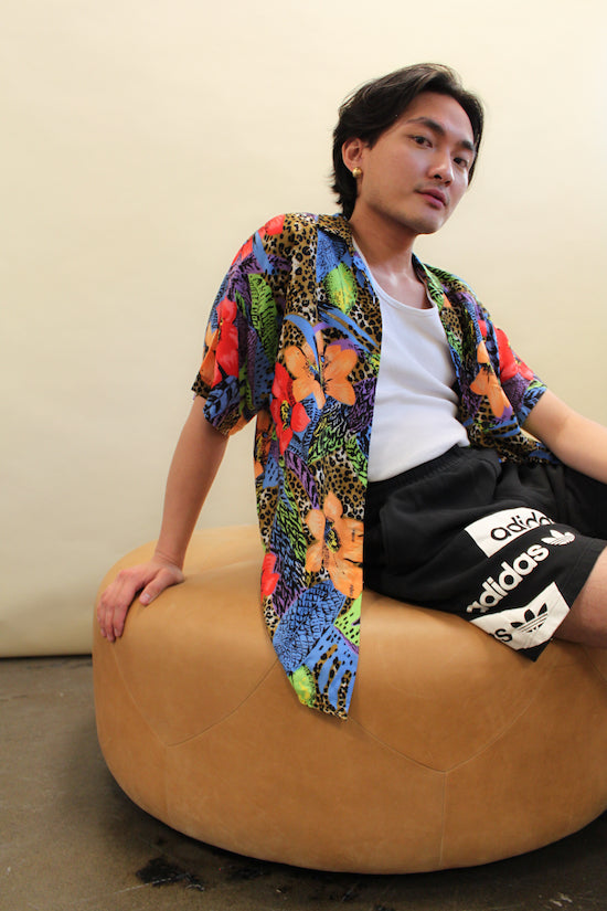 Man sits wearing a vintage patterned shirt and vintage black adidas athletic shorts