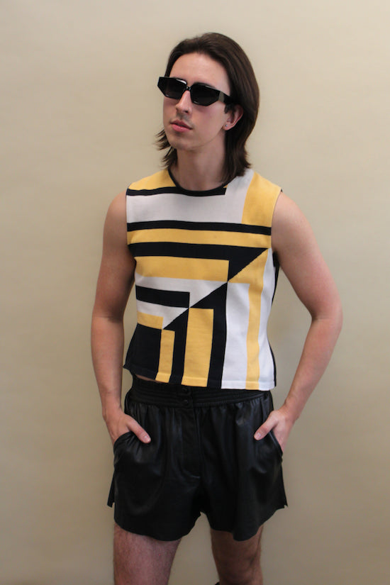 Non binary person in a geometric tank top and pleather shorts