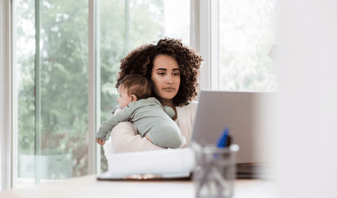 Mom holding baby with Separation anxiety while working on laptop