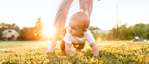 Baby crawling on grass with help