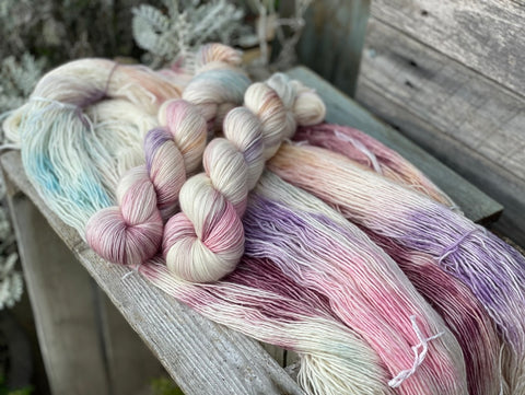 two skeins of hand dyed yarn sit on top of three loose skeins; they are cream with washes of various pastel shades