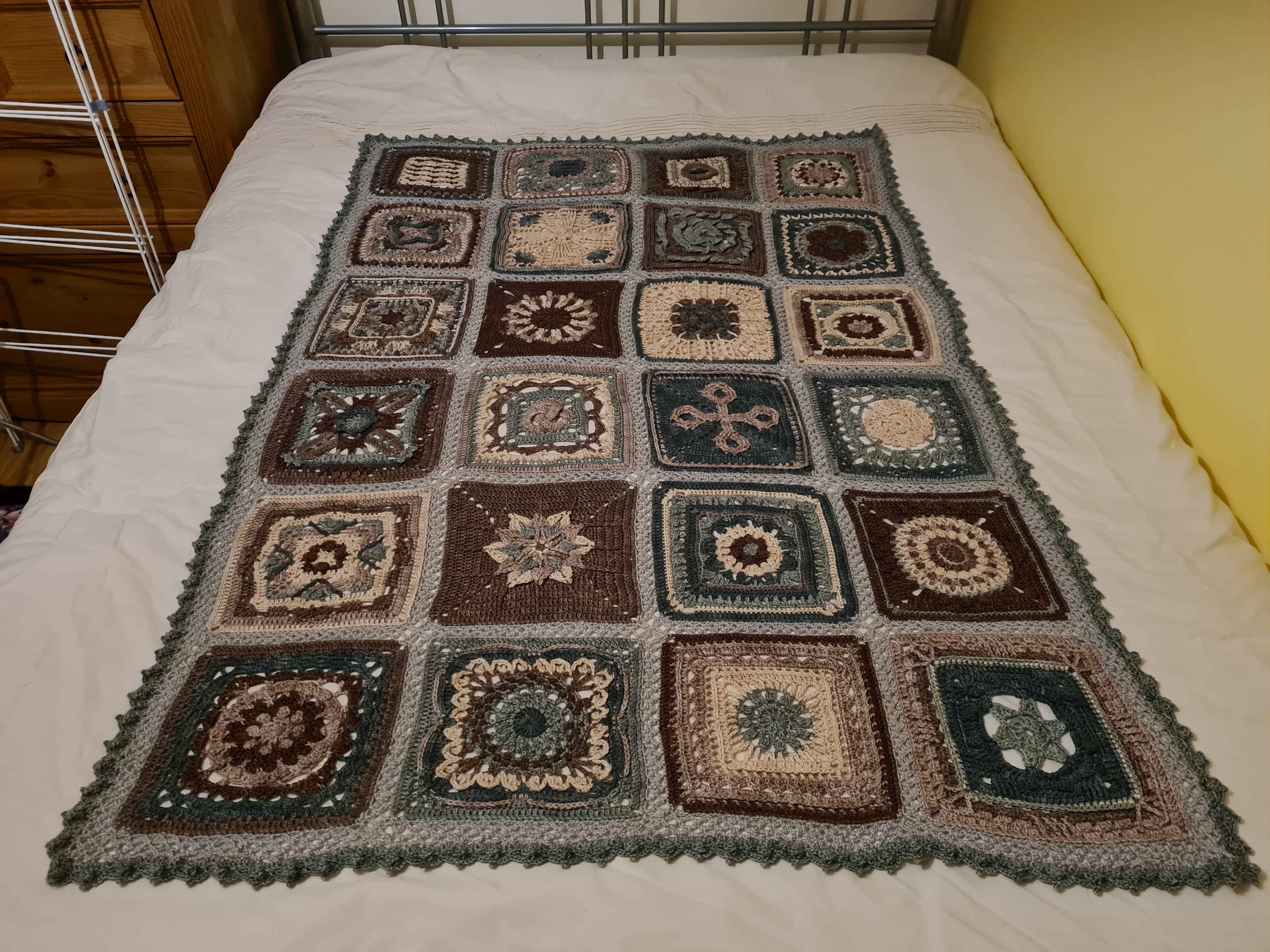 A medium sized blanket made up of intricate patterned blocks in shades of brown, blue and teal.