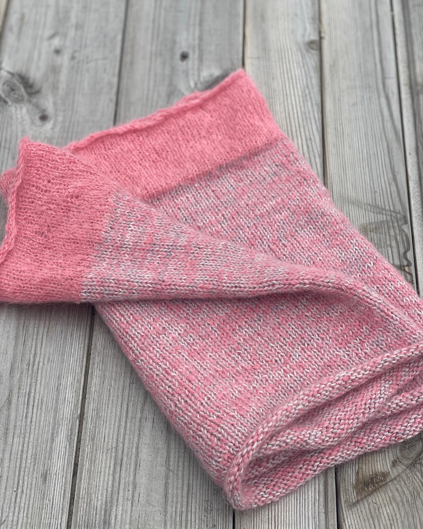 A pink and grey cowl lies on a table and is folded in half lengthways