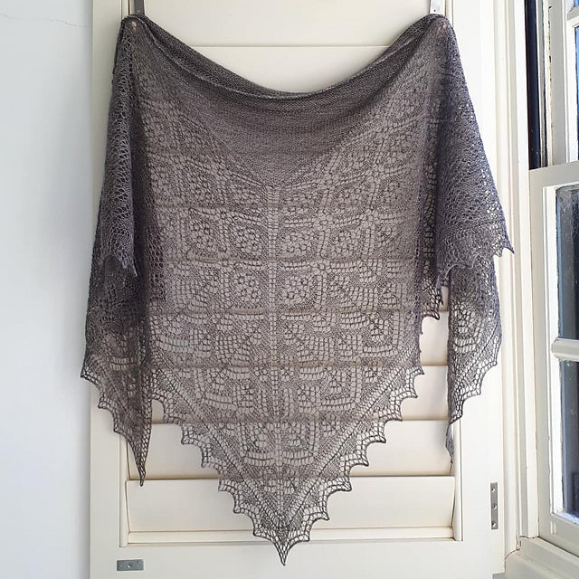 An intricate lace shawl in a dark grey colour hanging in front of a door