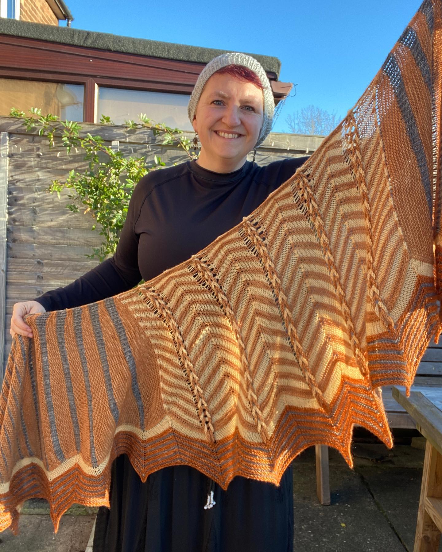 Victoria holding a shawl outstretched. The shawl features stripes and chevrons in light brown, brown a black.
