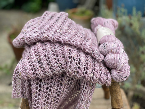 A lacy scarf and a skein of matching tweed yarn on a wooden stool