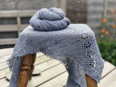 A shawl and a skein of denim blue yarn on a stool