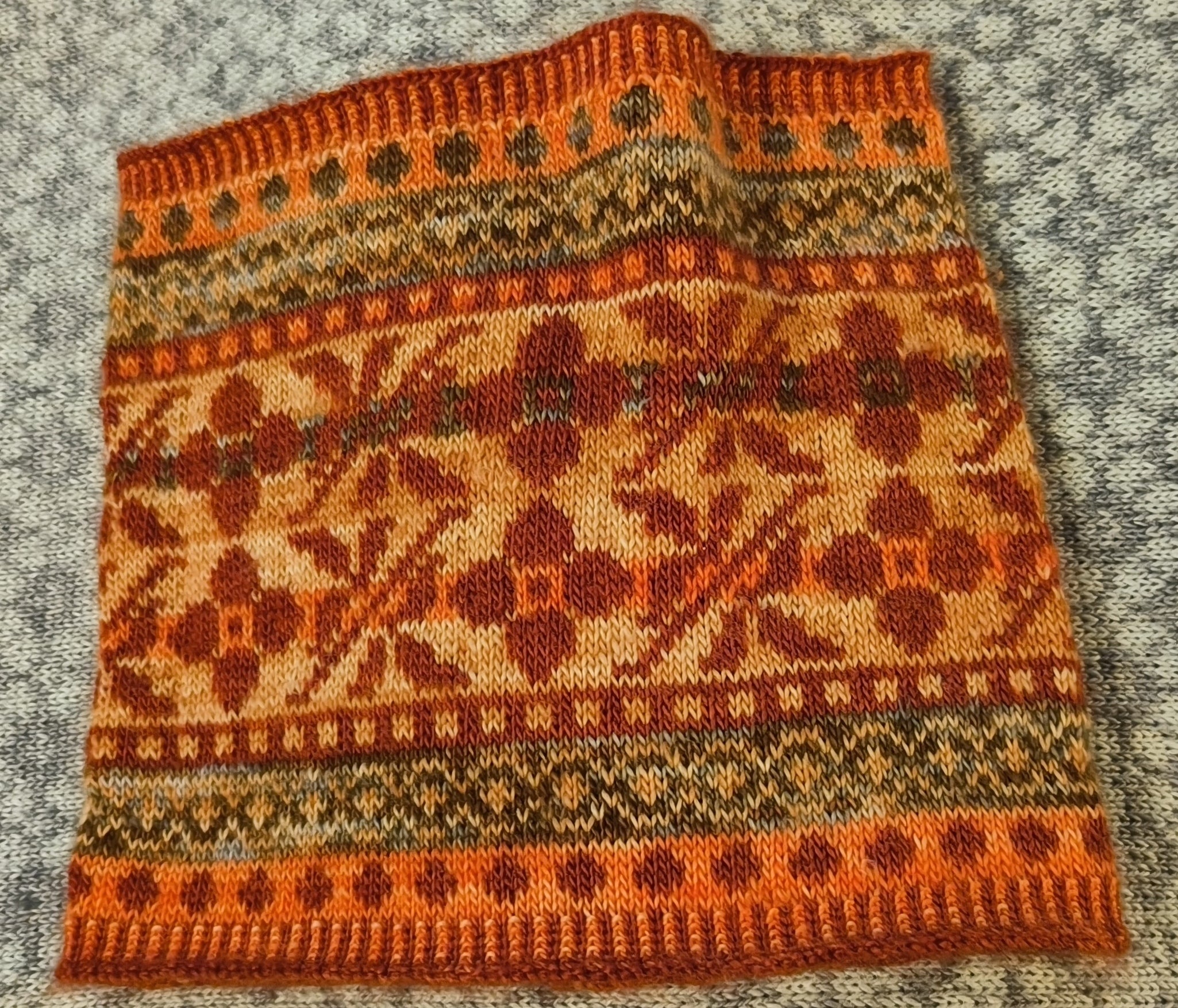A detailed colourwork cowl in shades of orange, red and brown