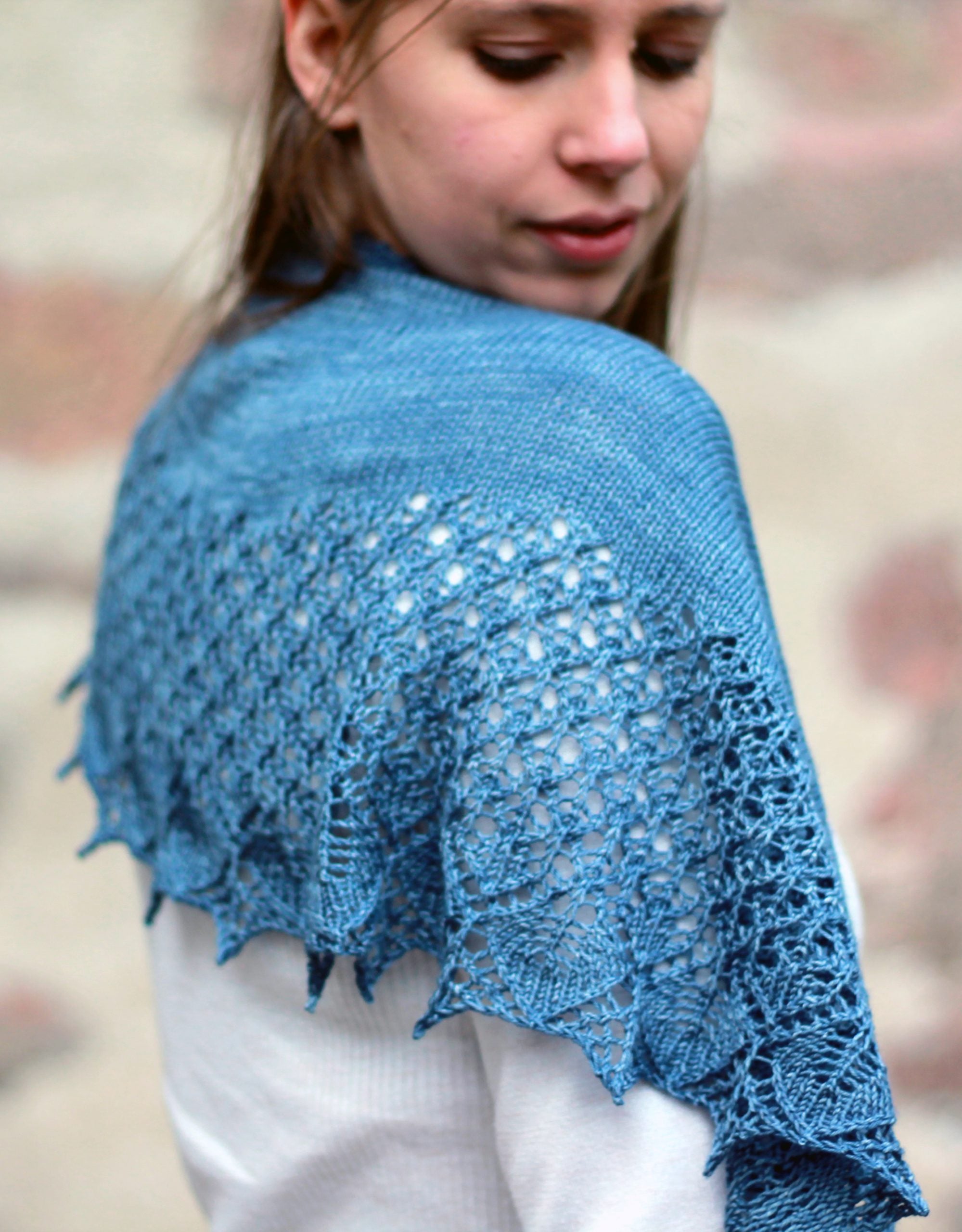 A person stood side on to the camera wearing a white top and a blue shawl draped over their shoulders. The shawl has a solid section closest to the neck and the bottom half is a lace pattern
