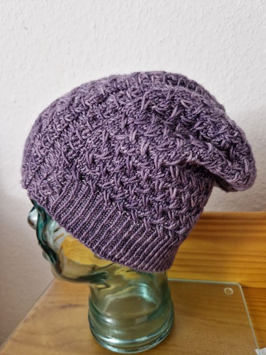 A purple hat with interesting stitch pattern details, displayed on a glass head