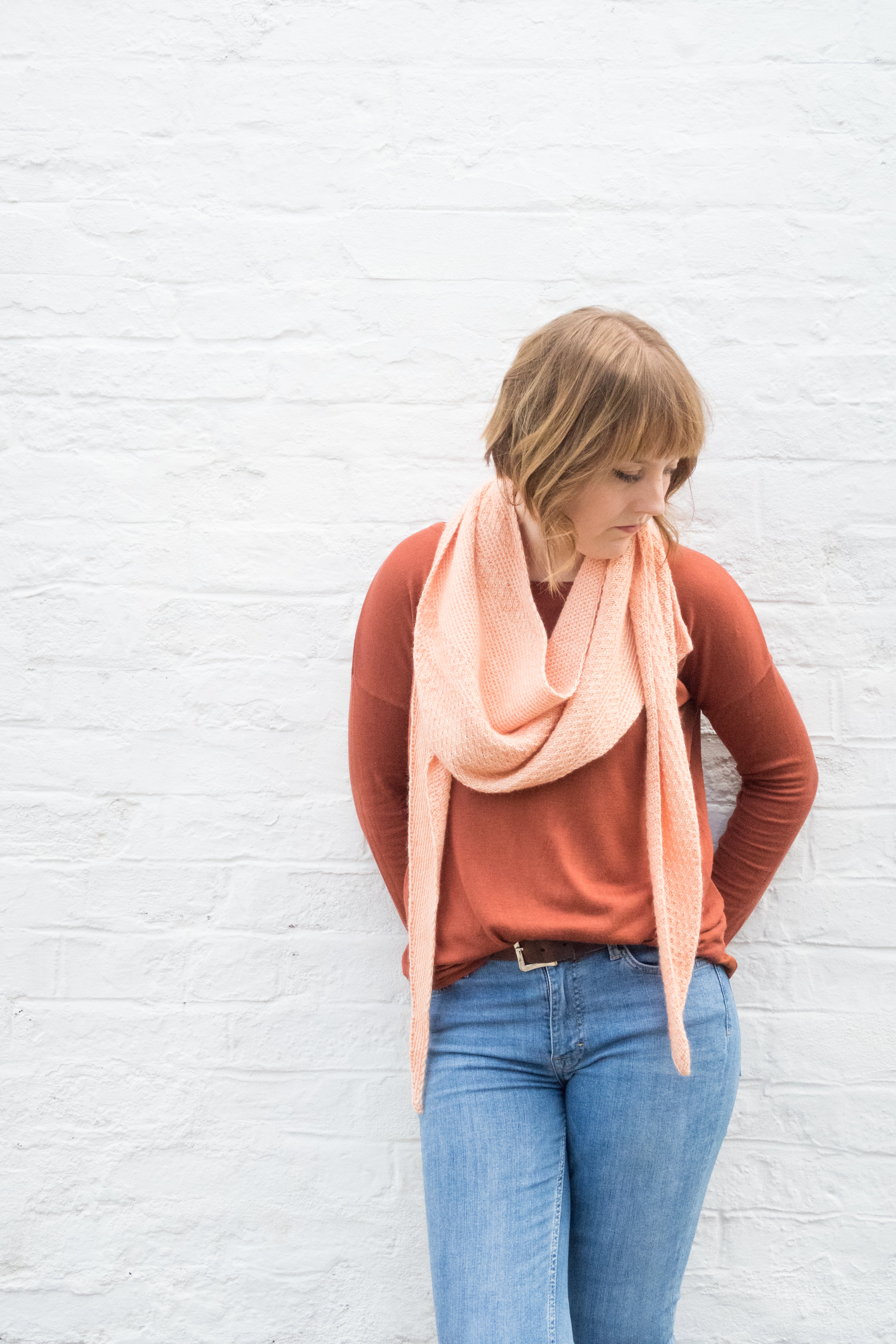 A person stood against a plain background wearing a peachy orange shawl wrapped around their shoulders