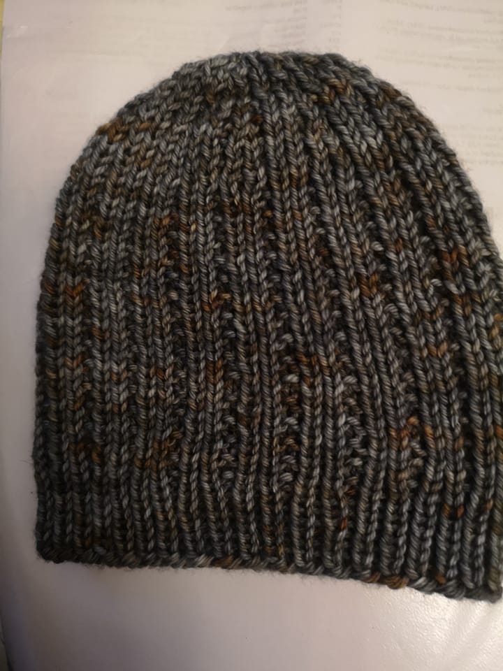 A grey and brown knitted hat resting on a beige surface