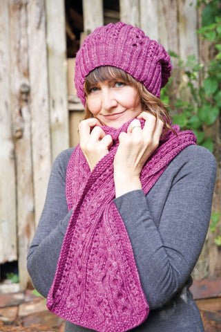 A person wearing a grey top and a deep purpley pink scarf and hat.