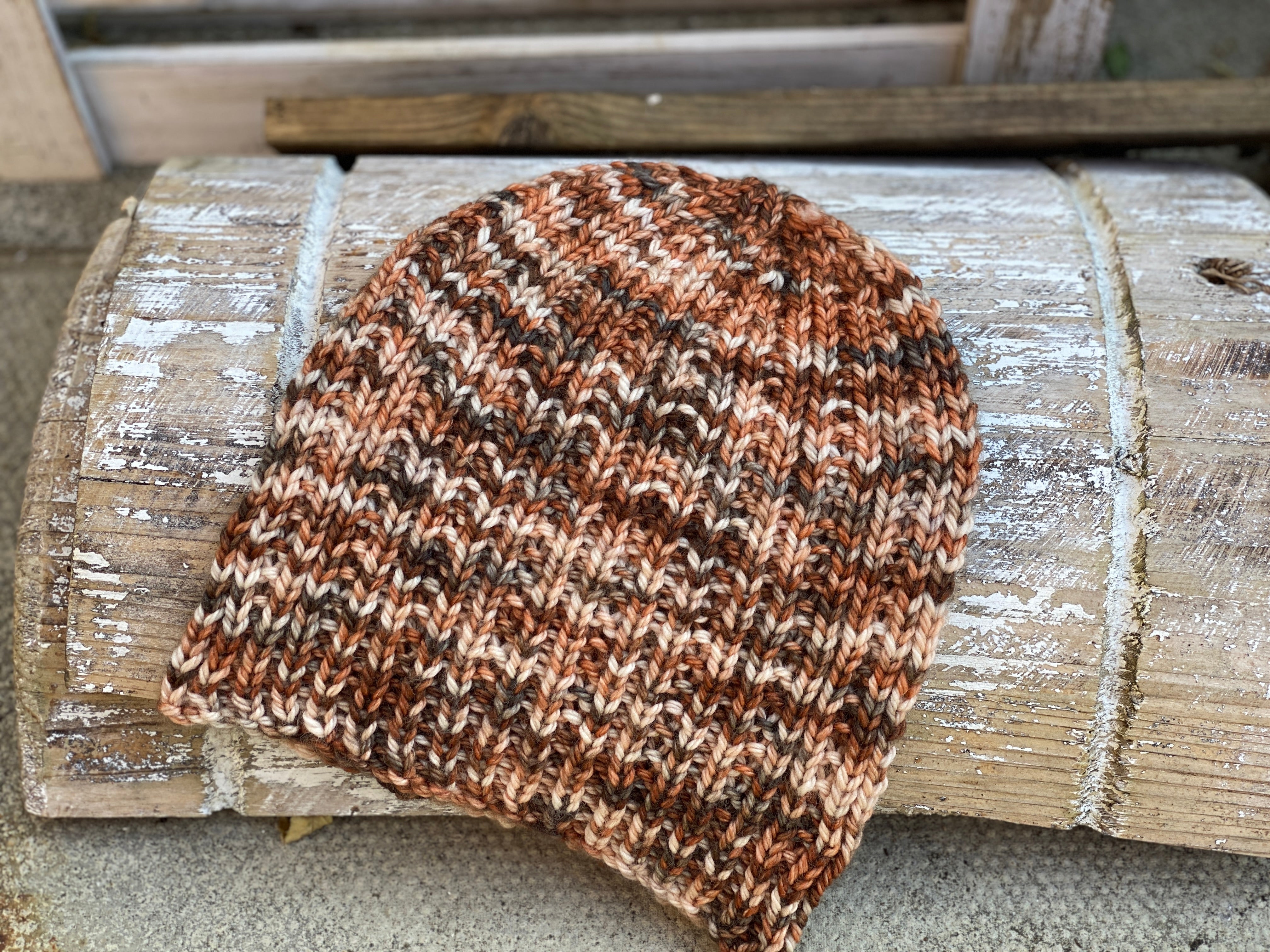 A knitted hat in shades of brown and cream resting on a wooden surface