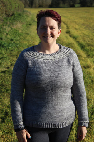 portrait of a woman wearing a handknit grey sweater with cream detailing around the neck and sleeves