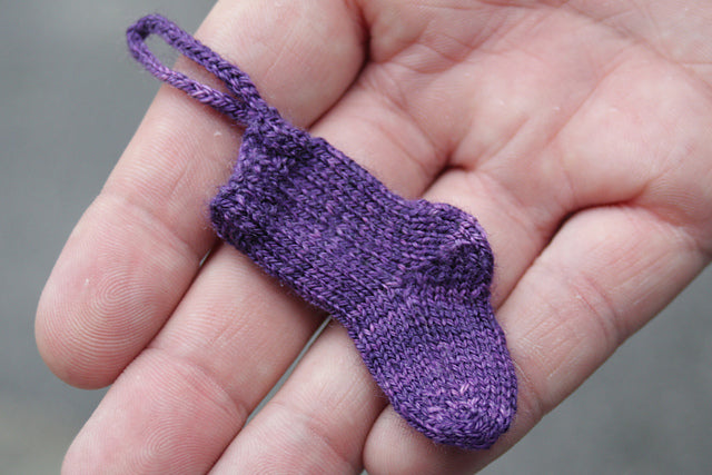 A tiny purple knitted sock resting on the fingers of a hand