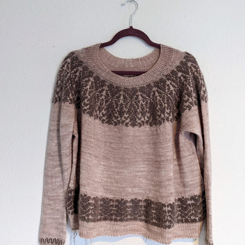 A pink jumper with brown lace detailed yoke and waist hanging on a wall