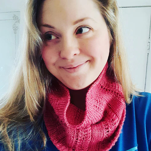 Hanna smiling and looking to the side of the camera, wearing a pink knitted cowl and a blue top