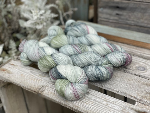 Three skeins of hand dyed yarn in soft green, grey and cream shades.