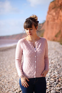 A person stood on a beach wearing a pretty pink cardigan with dandelion lace detail