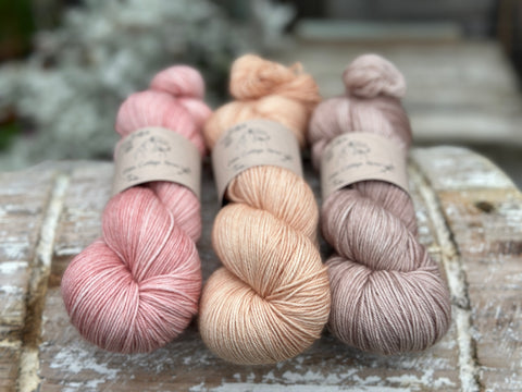 Three skeins of hand dyed yarn in soft pink, soft orange, and light brown