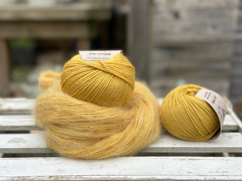 a swirl of golden yellow fluffy yarn along with two balls of smooth yarn in a matching golden yellow