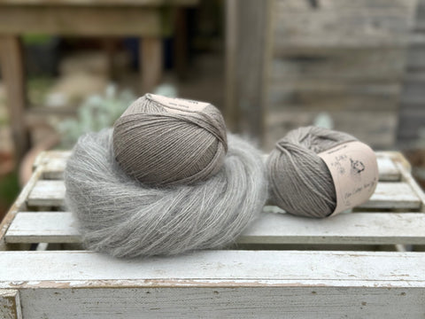 a medium grey swirl of fluffy yarn is next to two balls of smooth medium grey yarn